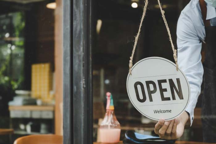 restaurant window with person turning over sign reading "open"