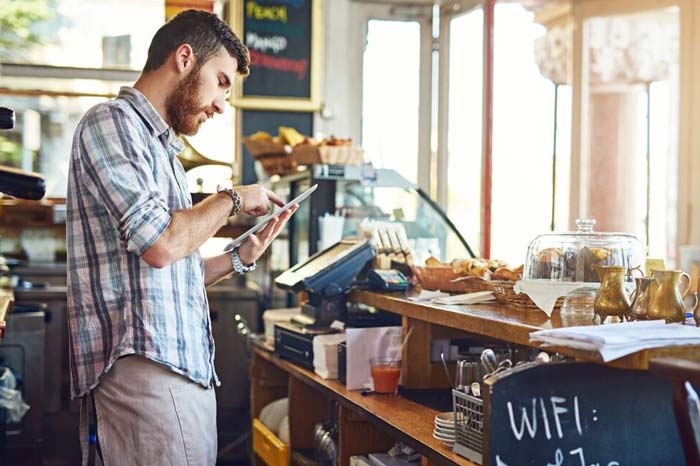 man working in café working on a tablet standing behind the counter